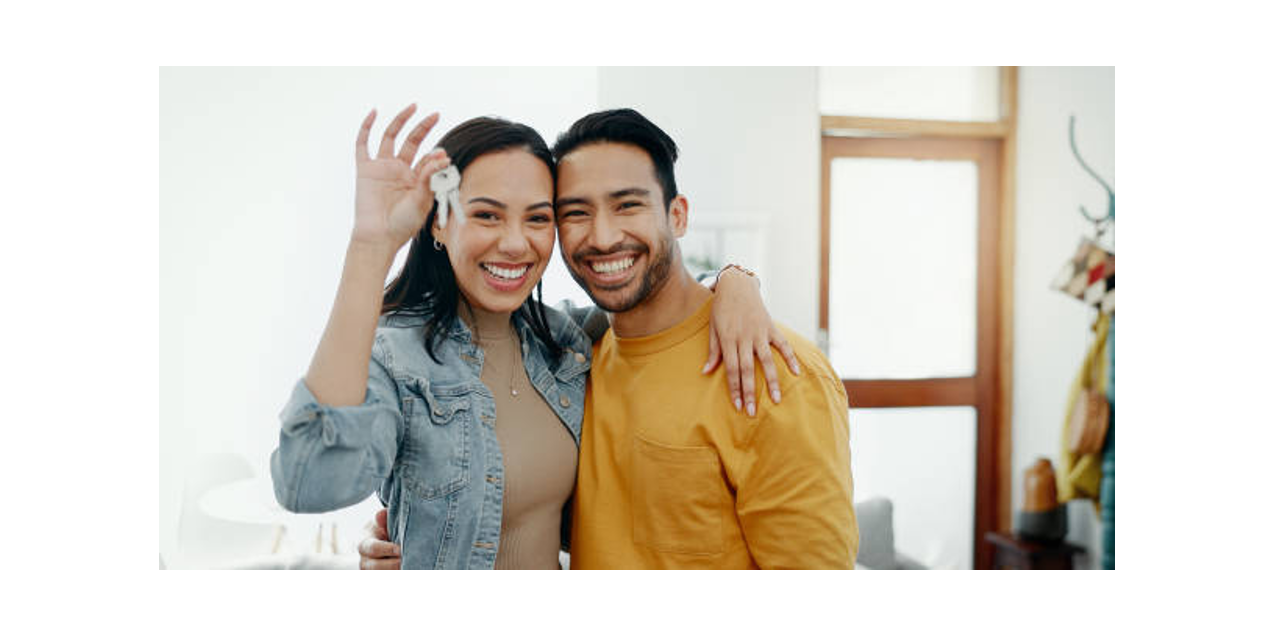 Happy young couple smiling as woman holds up house keys, celebrating new home ownership together.