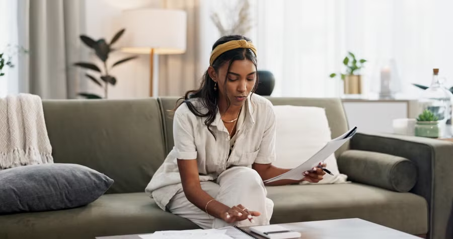 Woman with yellow headband reviewing documents on a green sofa in a bright, modern living room.