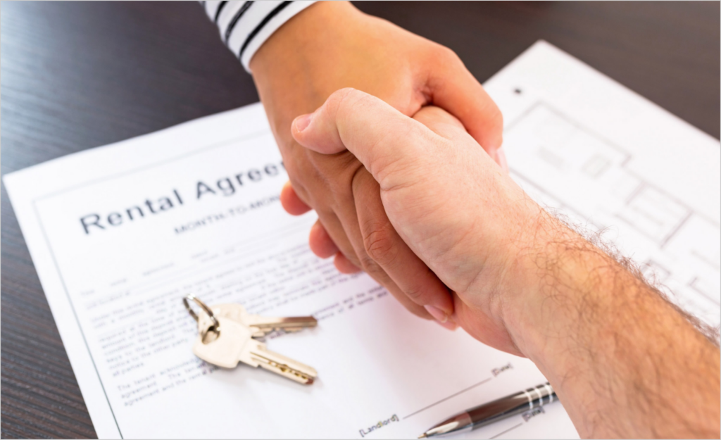 Two people shaking hands over a rental agreement document with keys and a pen on the table.